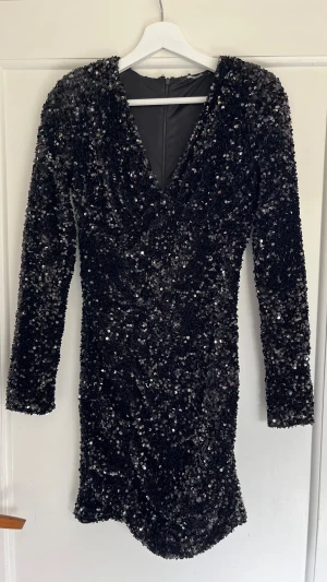 Svart paljettklänning Gina Tricot - Säljer en svart kort paljettklänning från Gina Tricot. Klänningen har v-ringning, långa ärmar och är täckt av glittriga paljetter. Perfekt för nyår🥰