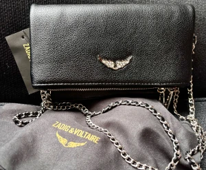Snygg väska från Zadig&Voltaire! - Svart mångsidig väska från Zadig&Voltaire av Rock Nano Grained Leather med många fack och snygga detaljer. Den avtagbara kedjan, som ger en edgy look, kan varieras så den kan bäras både som crossbody bag, clutch eller axelväska. Mått:  22 x 13 cm. Ny med tag.
