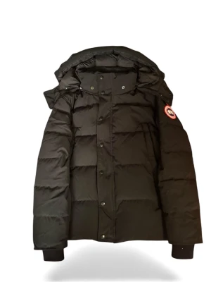 Svart pufferjacka från Canada Goose - Säljer en svart pufferjacka från Canada Goose med ikonisk patch på ärmen. Jackan har huva, dragkedja och knappar framtill, samt ribbade muddar vid ärmslut. Perfekt för kalla dagar och har en clean, stilren look. Modellen är Fusion S/P.