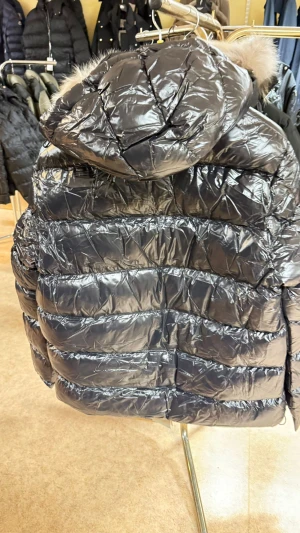 Ralph Lauren gorham glossed  - Svart, glansig pufferjacka från Polo Ralph Lauren med röd logga på bröstet. Jackan har huva, flera dragkedjeförsedda fickor och quiltad design. Materialet är syntet och dun, perfekt för kalla dagar. Stängs med dragkedja framtill och har långärmade ärmar.