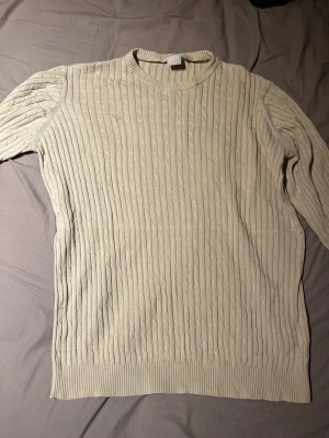 Beige ribbad stickad tröja Esprit - Säljer en beige stickad tröja från Esprit med ribbad struktur och rund hals. Tröjan har långärmade ärmar och breda muddar vid nederkant och ärmslut. Perfekt för dig som gillar klassisk och enkel stil med lite extra textur. Passar mer som M