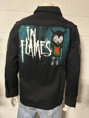 Jacka med In flames. Storlek XL. - Helt ny jacka med In flames. Storlek XL. Material i bomull. Kraftig dragkedja. Broderade patches på ärmarna. Tryck mönster på ryggen.