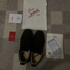 Svarta sneakers från Christian Louboutin - Säljer ett par svarta sneakers från Christian Louboutin med ikonisk röd sula och rund tå. Skorna har snörning och är tillverkade i skinn med beige innersida. Perfekt för dig som vill ha en lyxig och stilren look med exklusiva detaljer.