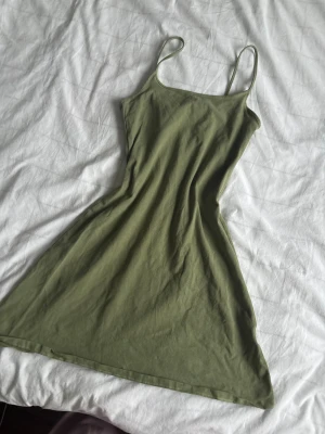 Olivgrön kort klänning från H&M Divided - Säljer den sötaste olivgröna klänningen som är perfekt till sommaren som slutar över knäna. Använd typ tre gånger. Och den är tjock i materialet. Så det gör att den inte är genomskinlig. PRISET KAN DISKUTERAS!!