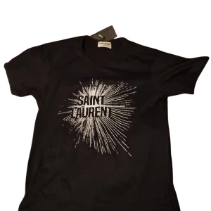 Svart Saint Laurent t-shirt med tryck - Sällsynt t-shirt från Saint Laurent med coolt vitt grafiskt tryck på bröstet. Helt oanvänd, endast testad. Priset är inte hugget i sten, pm för frågor.