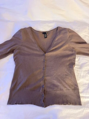 Söt Brun korta  - Snygg beige kofta från H&M i storlek L. Den har v-ringad hals, långa ärmar och knappar hela vägen framtill. Materialet är mjukt och tunt, perfekt för lager-på-lager. Ribbad kant nedtill och vid ärmslut ger en schysst detalj. 
