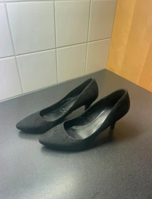 Svarta pumps med spetsig tå, storlek 40 - Säljer ett par klassiska svarta pumps i mockaimitation med spetsig tå och låg klack. Perfekta för dig som gillar stilrena och tidlösa skor. Passar storlek 40 och har en elegant siluett som lyfter vilken outfit som helst. Små i storleken så 38-39 skulle jag uppskatta storleken till. 