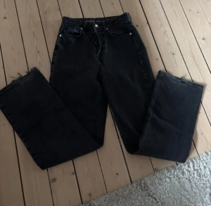Svarta wide jeans, regular fit, 26/32 - Svarta jeans med wide fit och regular midja, storlek 26 och längd 32. Klassisk femficksmodell med råa, fransiga benslut för en cool vibe. Perfekta om du gillar lite bredare ben och avslappnad stil.