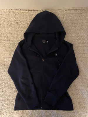 Ralph lauren hoodie  - En snygg Ralph Lauren hoodie med en mindre skada vid fickan som knappt syns. Köpt på Johnells i Linköping för ca 6 månader sedan men efter den revs lite så har den legat i garderoben. Kom gärna med bud eller frågor!