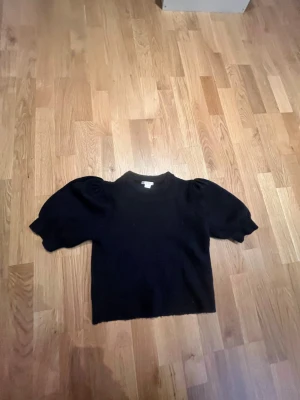 Svart stickad tröja med puffärm Gina Tricot - Svart stickad tröja från Gina Tricot i storlek 146/152. Tröjan har korta puffärmar med ribbade muddar och en rund halsringning. Mjuk och skön, perfekt för dig som gillar enkel men snygg stil. Passar dig som vill ha något klassiskt med en twist.