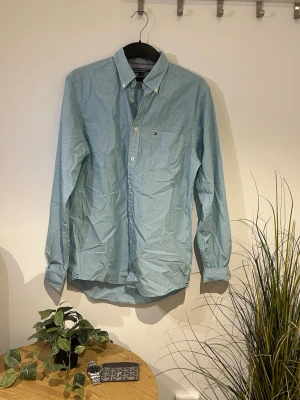 Blå randig skjorta från Tommy Hilfiger - Snygg Blå/grön Skjorta från Tommy Hilfiger. Den är i storlek S, och passar våran moddel fint som är 179cm🤗 Den är i fint skick, och själv klart så stryker vi skjortan innan vi skickar iväg den🤟🏻