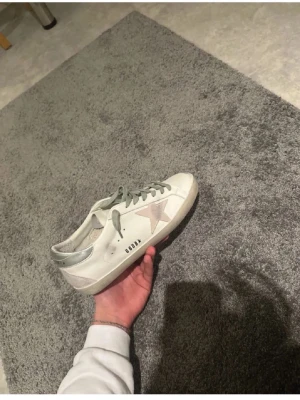 Golden Goose vita sneakers med stjärna - Golden Goose sneakers i vitt skinn med ljusgrå snörning och silverdetalj på hälen. Sidan har en beige mockastjärna och platt svart sula. Snygg, klassisk modell med rund tå. Skicket är 10/10 og följer med. Pris kan även diskuteras vid snabbaffär. Bara skriva vid funderingar och med bilder😊 