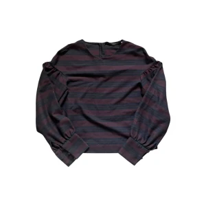 Randig blus med puffärm - Mörkblå och vinröd randig blus med långa puffärmar och breda manschetter. Blusen har rund halsringning och stängs med dragkedja bak. Perfekt för dig som gillar en stilren men ändå cool look.