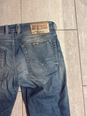 Blå jeans från Diesel Industry - Säljer ett par klassiska blå jeans från Diesel Industry med snyggt slitna detaljer och raka ben. Jeansen har fem fickor, ljus tvätt och tydliga sömmar. Passar dig som gillar en avslappnad och tidlös stil.