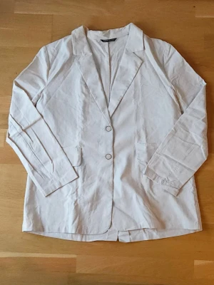 Beige kavaj - Snygg beige kavaj med klassisk krage, två knappar framtill och dekorationsfickor. Långärmad och rak passform, perfekt för dig som gillar stilrena och chill plagg. Passar till både jeans och dressade byxor.