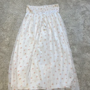 Vit blommig långkjol från Gina Tricot - Superfin långkjol från Gina Tricot i vit med små rosa blommor. Kjolen har smock i midjan, knytband med tofsar och är gjord i ett lätt, luftigt material. Perfekt för en somrig look med romantiska vibes. Kontakta för fler bilder💞