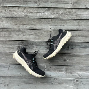 Svarta Asics sneakers med vit sula - Snygga svarta Asics sneakers med vit och beige sula. Skorna har mesh- och syntetmaterial, klassisk Asics-logga på sidan och svarta snören med vita prickar. Perfekta för dig som gillar sportig stil och vill ha bekväma skor till vardagen.