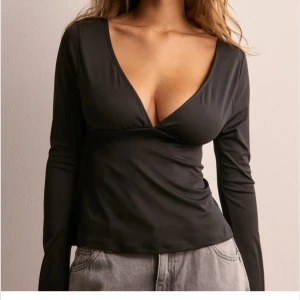 Svart långärmad topp med rosett - Säljer en svart långärmad topp från NA-KD med djup v-ringning framtill och öppen rygg med en snygg rosettdetalj. Aldrig använd.