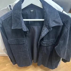 Mörkblå manchesterjacka från Uniqlo - Säljer en mörkblå overshirt från Uniqlo i mjuk manchester. Jackan har klassisk krage, två stora bröstfickor med knappar och raka ärmar. Perfekt för lager-på-lager och ger en chill vibe till din outfit.