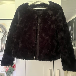 Svart pälsjacka från Vero Moda - Mysig svart pälsjacka från Vero Moda med rund halsringning och knäppning framtill. Jackan har lång ärm och är tillverkad i ett mjukt, fluffigt material som ger en lyxig känsla. Perfekt för dig som vill ha en trendig och varm look.