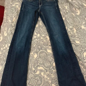 Blå bootcut jeans från Gina Tricot - Snygga blå jeans från Gina Tricot i bootcut-modell med kontrastsömmar. Klassisk femficksdesign och normal passform. Jeansen är tillverkade i denim och har en mörk tvätt som ger en cool look.