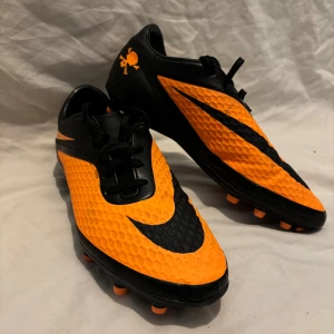 Nike Hypervenom Phantom (1st gen) - Säljer ett par klassiska Nike Hypervenom Phantom i färgen svart/orange (Skull Edition). Skorna är i fint skick och redo för spel. En eftertraktad modell som inte längre tillverkas – perfekt för dig som vill sticka ut på planen eller samla på ikoniska fotbollsskor.  ✅ Storlek: 41 ✅ Bra skick ✅ Bekväm passform & grym touch  Pris: 1 800 kr (eller bud) 