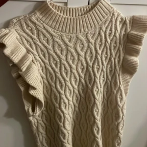 Stickad  tröja med volang - Supersöt stickad  tröja i beige med grovt kabelstickat mönster och bred ribbad krage och Volangdetaljer, storlek 155-165 men den är jättestor i storlek så den är som en M/L, prislapp kvar & nypris 299