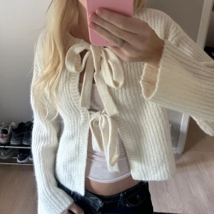 Vit stickad kofta med knytband - Säljer en supersöt vit stickad kofta med två stora rosetter då den inte kommer till användning!! Funkar att ha både utan linne under och med. <333
