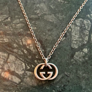 Gucci halsband med GG-logo i silver - Snyggt halsband från Gucci i silverfärgad metall med den ikoniska GG-loggan som hänge. Kedjan är klassisk och passar perfekt till streetwear eller en mer stilren look. Ett statement-smycke för dig som gillar exklusiva accessoarer.