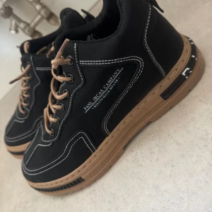 Svarta sneakers med bruna detaljer - Säljer ett helt nya svarta skor som passar till våren. Helt nya har aldrig används! Storlek 41.