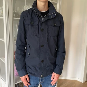 Mörkblå J.lindeberg Field jacka - S - Jag säljer den här superfina J.lindeberg field jackan. Den är i jättebra skick utan defekter och skador. Den är i storlek S. Modellen heter Bailey 62 Sports nylon. Tveka inte att höra av er!
