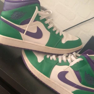 Nike Air Jordan 1 gröna/lila sneakers - Nike Air Jordan 1 sneakers i en riktigt fet färgkombo med grönt, lila och vitt. Klassisk high-top modell med lila swoosh och detaljer, gröna paneler och vit bas. Snygga lila sulor och vita skosnören. Perfekta för dig som vill sticka ut med dina kicks.