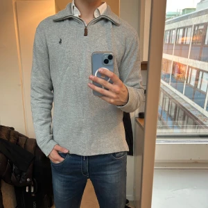 Polo Ralph Lauren half zip tröja - Klassisk grå långärmad tröja från Polo Ralph Lauren med half zip och liten broderad logga på bröstet. Tröjan har hög krage och är tillverkad i mjuk bomullsmix, perfekt för lager-på-lager. Enkel och stilren design som funkar året runt. Knappt använd, Skick 9/10.