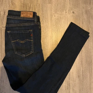 Mörkblå Replay jeans, storlek 28 - Snygga mörkblå jeans från Replay med klassisk femficksdesign och kontrastsömmar. Byxorna har en rak passform och är tillverkade i slitstarkt denim med Replay-logga på bakfickan och läderpatch i midjan. Perfekta för en stilren vardagslook.