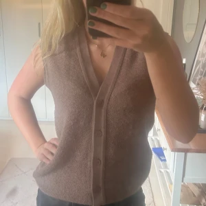 Brun stickad väst från Rodier Paris - Säljer en brun stickad väst från Rodier Paris med v-ringning och knappar framtill. Västen har en klassisk, rak passform och är tillverkad i ett mjukt, strukturerat material. Perfekt nu till hösten 