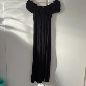 Svart offshoulder maxiklänning från H&M - Svart långklänning från H&M med offshoulder-modell och puffiga korta ärmar. Klänningen har rynkade detaljer upptill och en slits framtill. Tillverkad i ett mjukt, lätt material som ger ett snyggt fall.