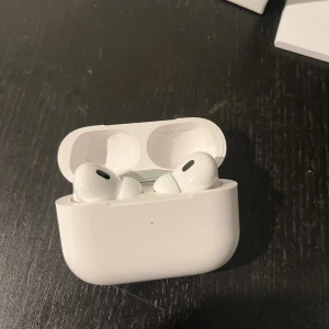 AirPods Pro 2 - Apple AirPods Pro i mycket fint skick, komplett med originalförpackning, laddningskabel och manual. Trådlösa hörlurar med aktiv brusreducering och laddningsetui. Inga synliga repor eller skador, ser knappt använda ut.
