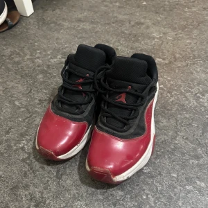 Svarta och röda Nike Air Jordans lows - Säljer ett par Nike Air Jordans i low-modell med svart mesh och rött skinn. Skorna har vit sula, klassisk Jumpman-logga och snörning. Perfekta för dig som gillar streetwear och vill sticka ut med snygga färgkontraster. Priset är diskutbart