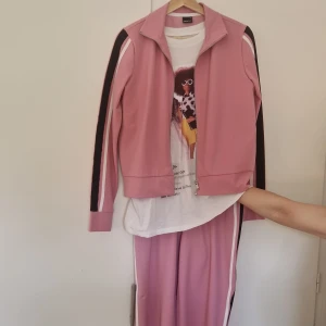 Rosa mjukisbyxor med revärer - Säljer ett par snygga rosa mjukisbyxor med svarta och vita revärer längs sidorna. Byxorna har en avslappnad passform och är perfekta för en chill och sportig look. Matcha med hoodie eller t-shirt för en cool vardagsstil.