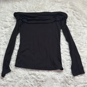 Svart offshoulder topp från H&M Divided - Svart långärmad offshoulder topp från H&M Divided i mjukt, tunnt och stretchigt material. Toppen har en bred, nedvikt kant över axlarna och smickrande passform. Perfekt för dig som gillar en stilren och enkel look med en twist. Köpte utomlands och tror ej den fortfarande säljs, aldrig använt.