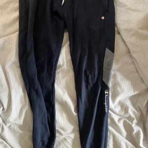 mörkblå mjukisbyxor  Champion - oanvända! Svarta mjukisbyxor från Champion med grå detalj på ena benet och logga längs vaden. Byxorna har dragsko i midjan och är tillverkade i mjukt bomullsmaterial. Perfekta för chill eller träning, med en slim passform och klassisk look.