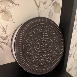 Oreo Cookie Box - Unik plåtburk i form av en Oreo-kaka, perfekt för förvaring av småsaker eller snacks. Burken är i gott skick med mindre yttre slitage, och har ett rent och rymligt inre. Perfekt som dekor eller present till Oreo-fans.
