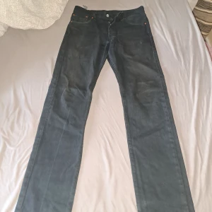 Levi's 501 svarta jeans W28 L32 - Klassiska svarta Levi's 501 jeans med raka ben och knappgylf. Jeansen har fem fickor och är tillverkade i slitstarkt bomullstyg. Perfekta för dig som gillar en tidlös och clean look.