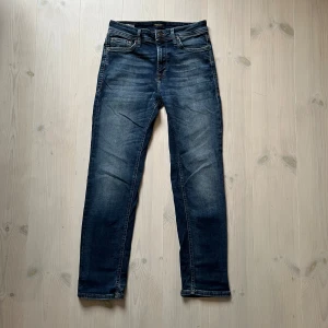 Jack & Jones Regular Clark jeans blå - Snygga blå jeans från Jack & Jones, modell Regular Clark. Klassisk femficksdesign med raka ben och normal passform. Jeansen har en mörkblå tvätt med lätt slitning och kontrastsömmar. Perfekta för en avslappnad och stilren look.