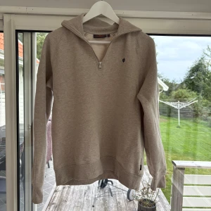 Beige half zip sweatshirt från Morris - Sonen säljer en mkt fin tröja. Beige sweatshirt från Morris med half zip och liten broderad logga på bröstet. Tröjan har hög krage, långa ärmar och är tillverkad i mjuk bomullsblandning. Perfekt för lager-på-lager under hösten eller våren. Mycket fint skick. Använd några gånger. Nu är den för liten för honom tyvärr.