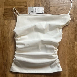 Vit festtopp Zara - Halv off shoulder topp från zara, helt oanvänd (testad en gång)  med lappen kvar! Säljer då den var lite för kort på mig som är väldigt lång. Helt utan defekter. 
