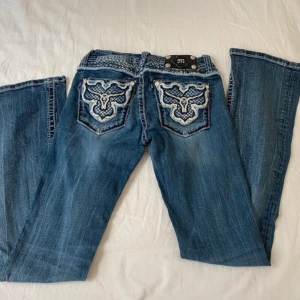 Vintage Miss Me jeans  - Snygga lågmidjade bootcut jeans från Miss Me med broderade bakfickor i vitt och blått, samt dekorativa nitar och detaljer. Storlek 27 men små i storlek, passar xxs/xs