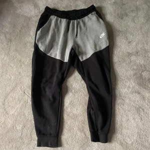 Nike tech mjukisbyxor svart och grå M - Nike mjukisbyxor i svart och grått med drag snören i midjan och ribbade muddar vid benslut. Byxorna har en sportig look med kontrastpaneler och klassisk Nike-logga på vänster sida. Perfekta för chill eller träning. Hör av dig vid frågor😁