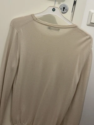 Beige tröja från J.Lindeberg - Säljer en stilren beige tröja i merinoull från J.Lindeberg i storlek M. Tröjan har rund halsringning, diskret logga på bröstet och är tillverkad i mjukt material. Perfekt för dig som gillar minimalistisk och clean stil.