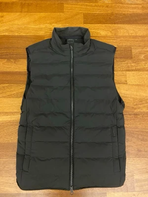 Svart dunväst från Didriksons, S - Säljer en svart dunväst från Didriksons i storlek S( Nypris 200€/ ca 2150kr) Västen har hög krage, quiltad design och dragkedja framtill. Insidan har 4 fickor och framsidan har 2. Perfekt för lager-på-lager och enkel att matcha. Är ni intresserade skickar jag gärna fler bilder och mer information om västen.